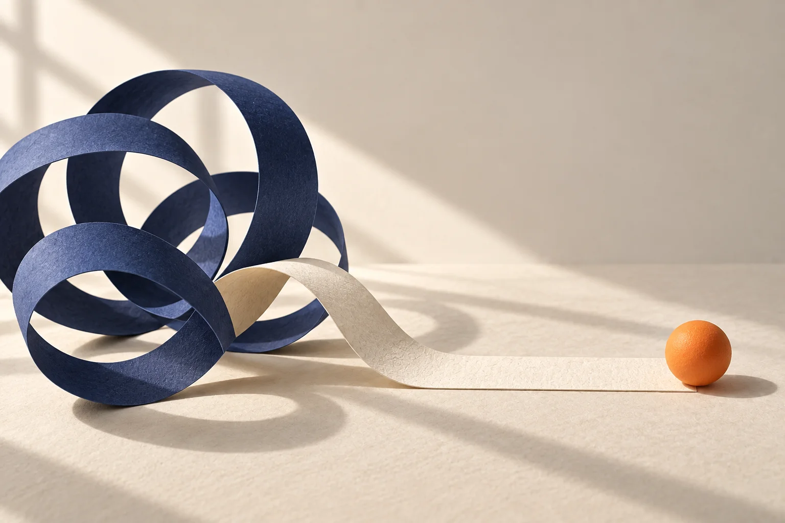 A navy paper loop beside a straight paper bridge and orange sphere.